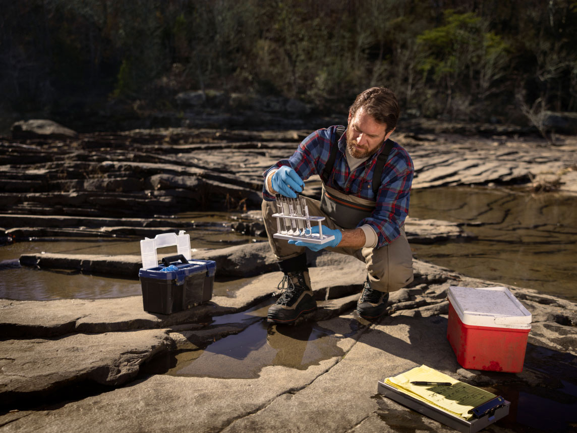 A man collecting samples of river water in test tubes in a forest preserve