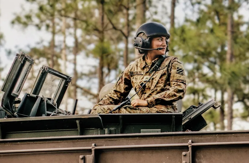 A U.S. Army Specialist poses for a photo in front of a CH-47 Chinook helicopter